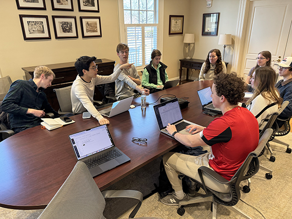 a group of students sit around a conference table in Cater Hall. Li is speaking to them with animated hands waving in the air