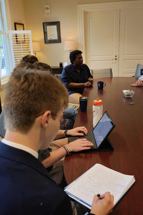 students sitting around a table listening to a speaker who is also sitting with students