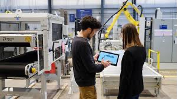a man and a woman look over a file next to robotics in a factory