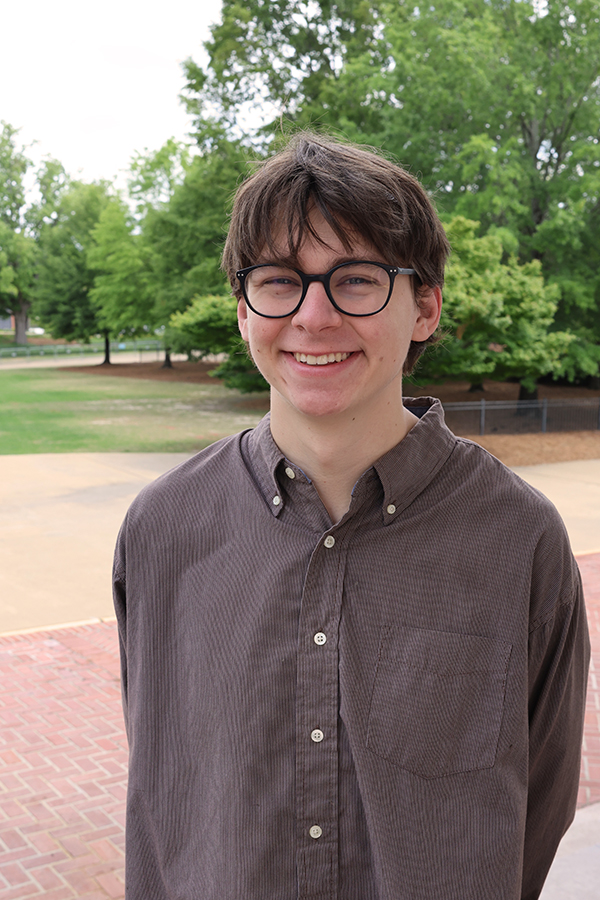 Will Lewis standing on Cater Lawn. Will has on a brown shirt and has brown hair and glasses