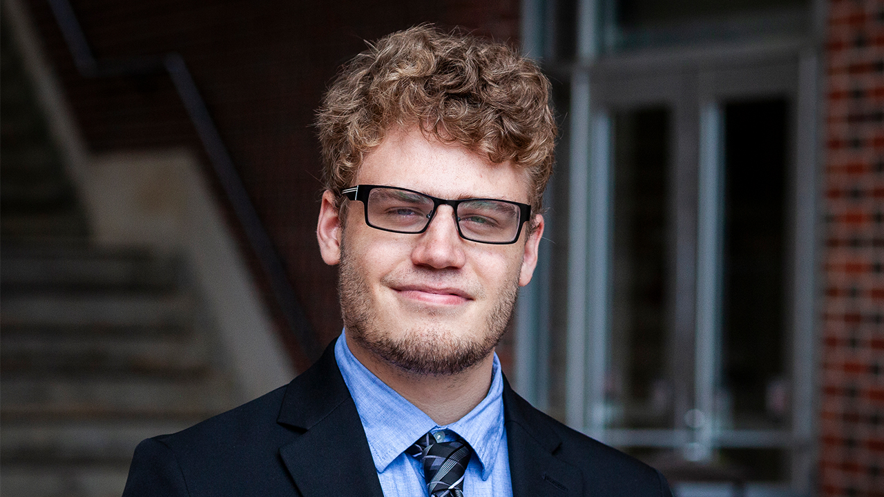 headshot of eirik mulder with a dark background. Eirik is in a blue suit and tie with glasses on