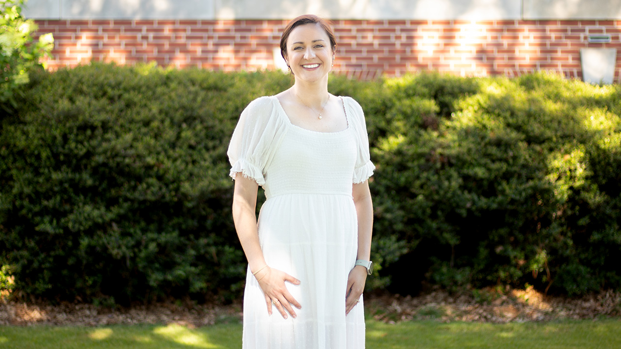 A woman wearing a white dress poses for a photo against a brick wall.