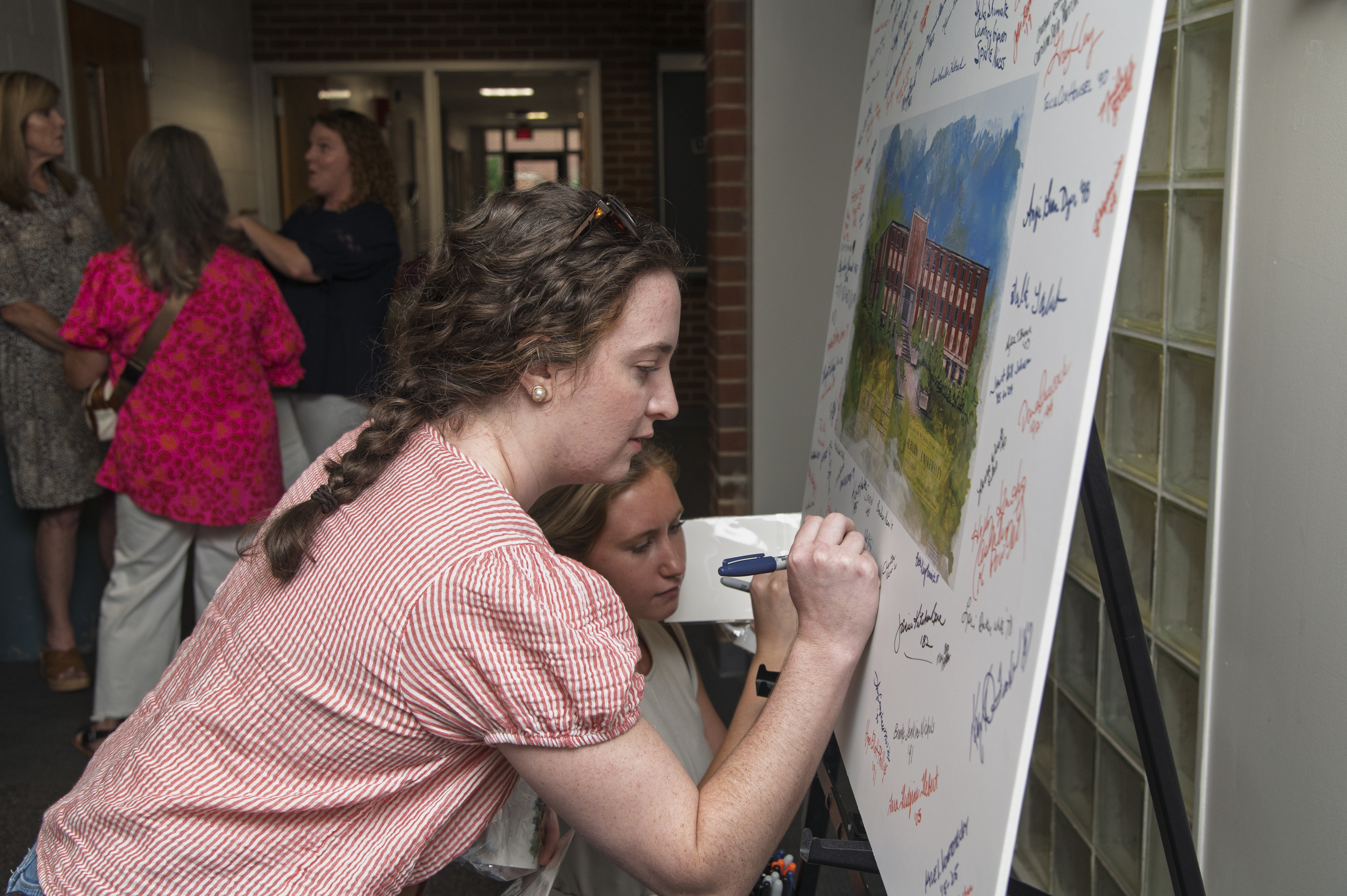 A guest leaves her signature on a watercolor painting of Spidle Hall 