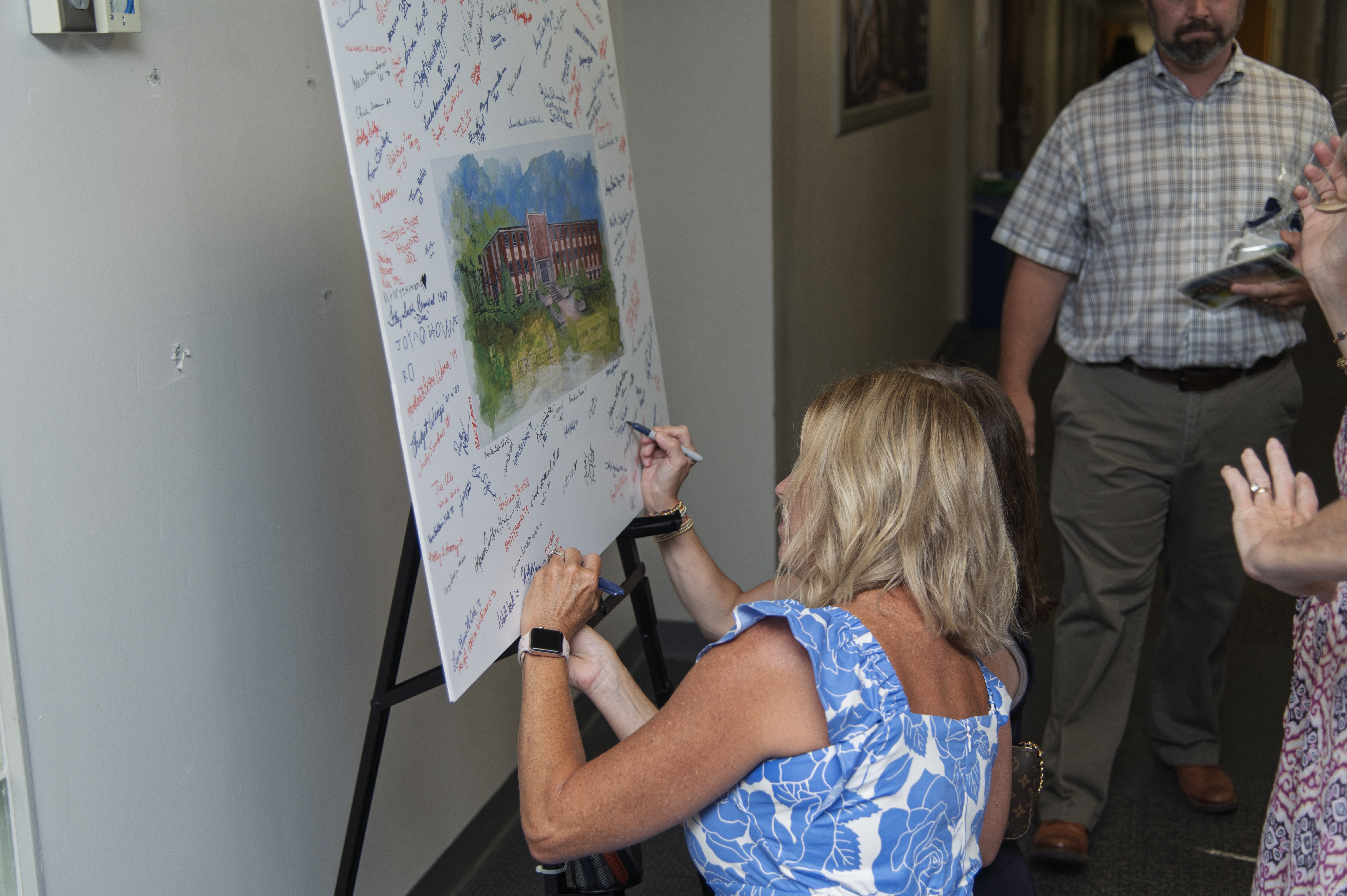 A guest leaves her signature on a watercolor painting of Spidle Hall 