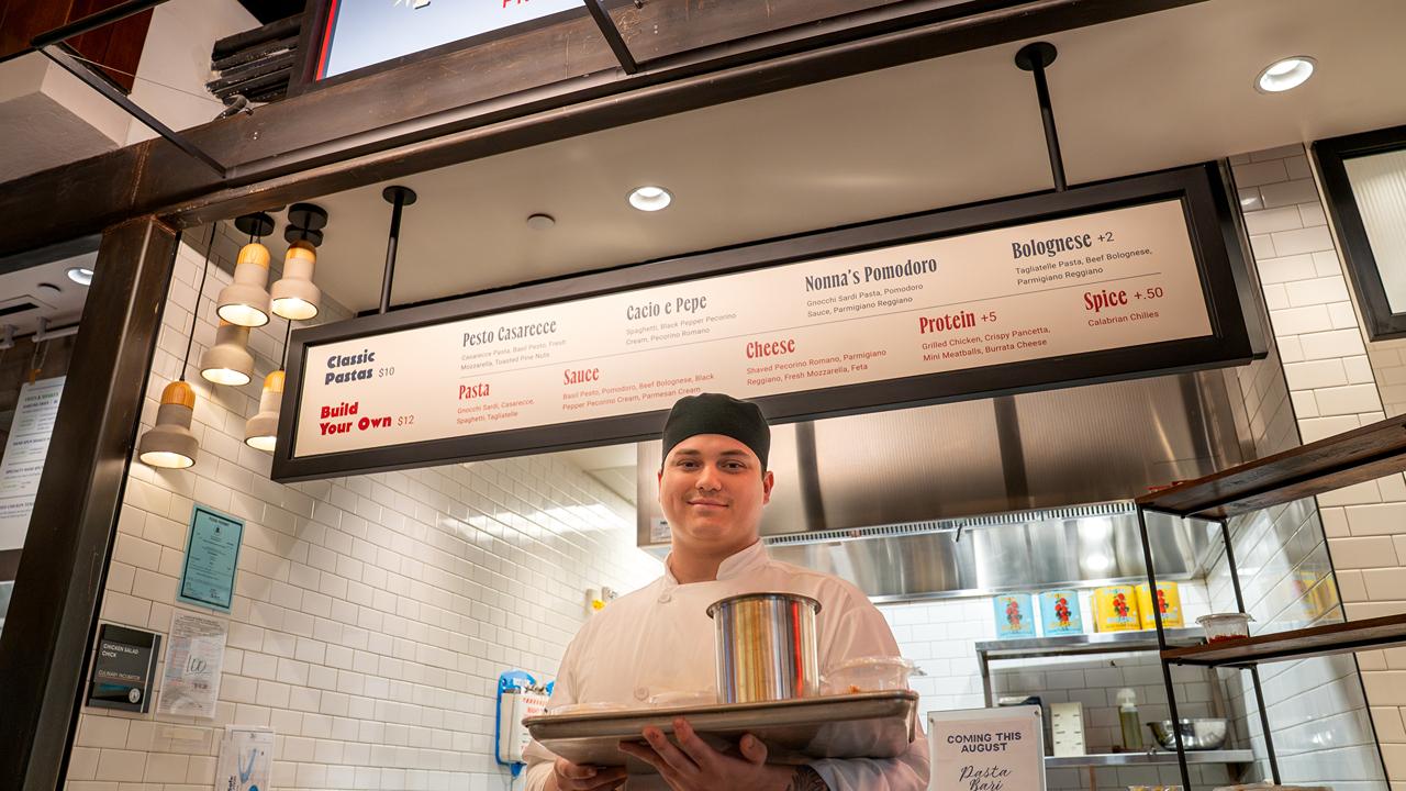 A student poses for a photo in front of Pasta Bari at the Incubator