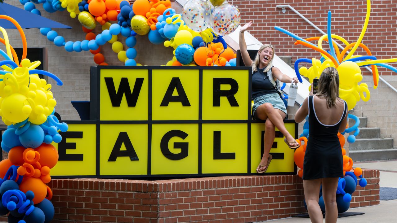 Students taking photos at a large War Eagle sign during a first week of class celebration