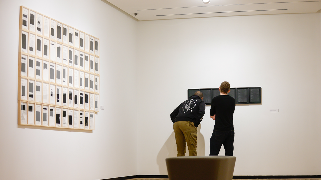 Two visitors examine a work of art in a gallery.