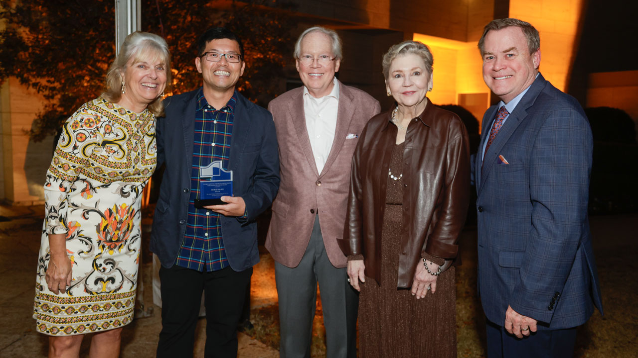Four people pose with an award receipient for a photo opportunity.