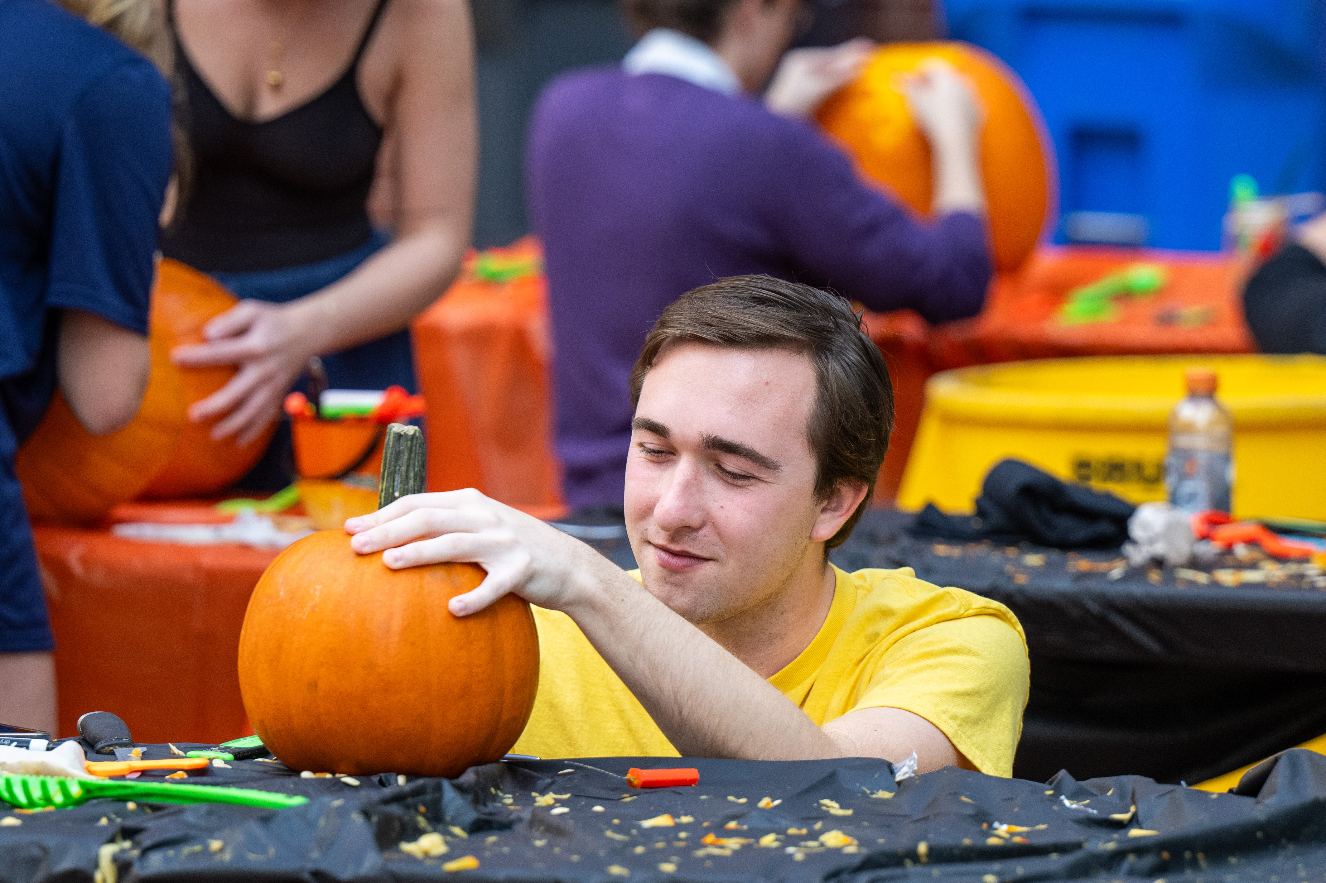 A young man focuses intently while carving a pumpkin