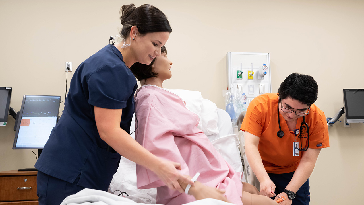 Two people in nurse uniforms work on a 'dummy' patient