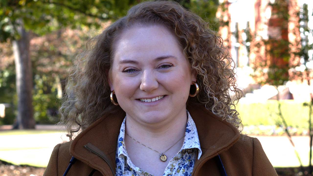 A woman stands smiling outside with a stethoscope around her neck