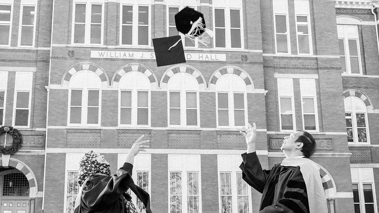 A man and woman toss graduation caps