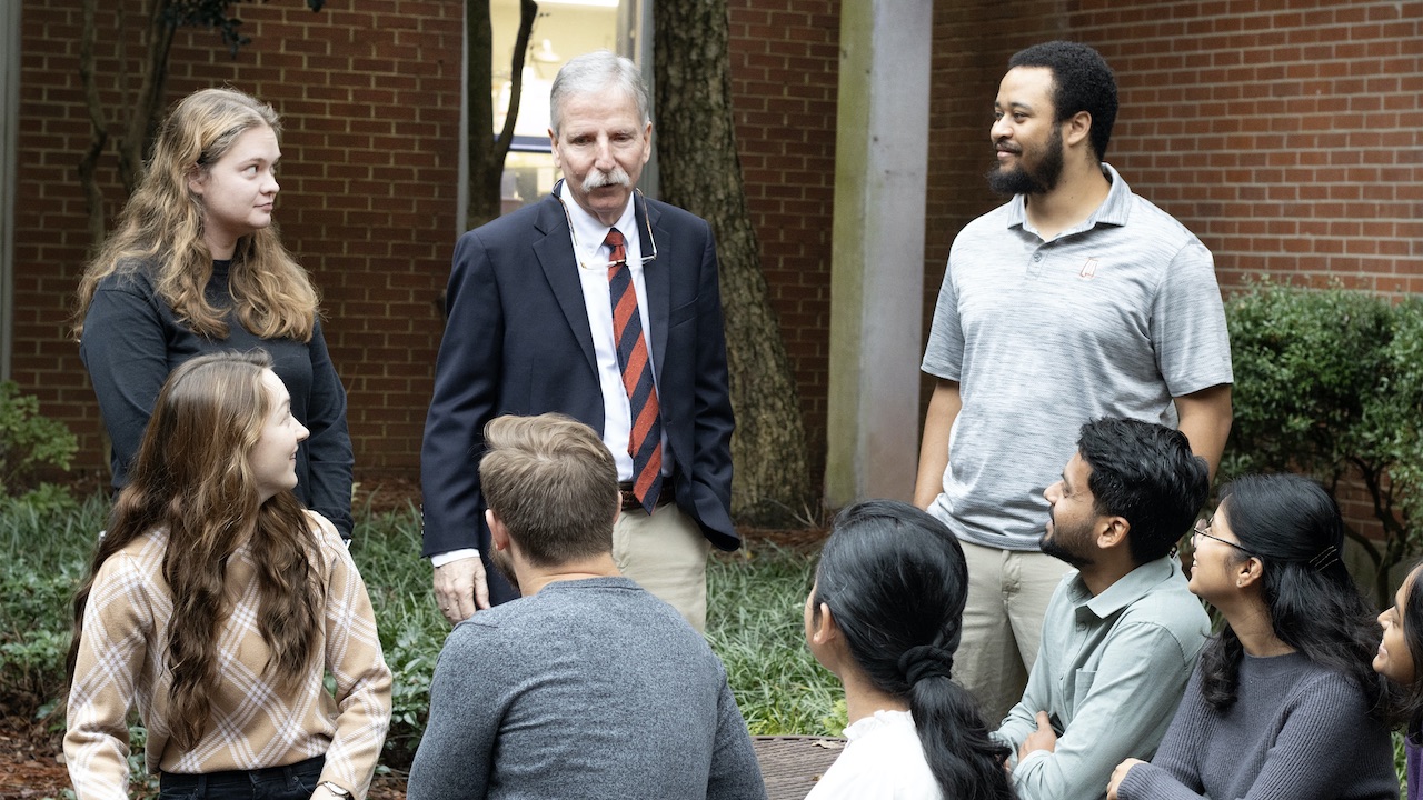 Older man surrounded by graduate students outside 
