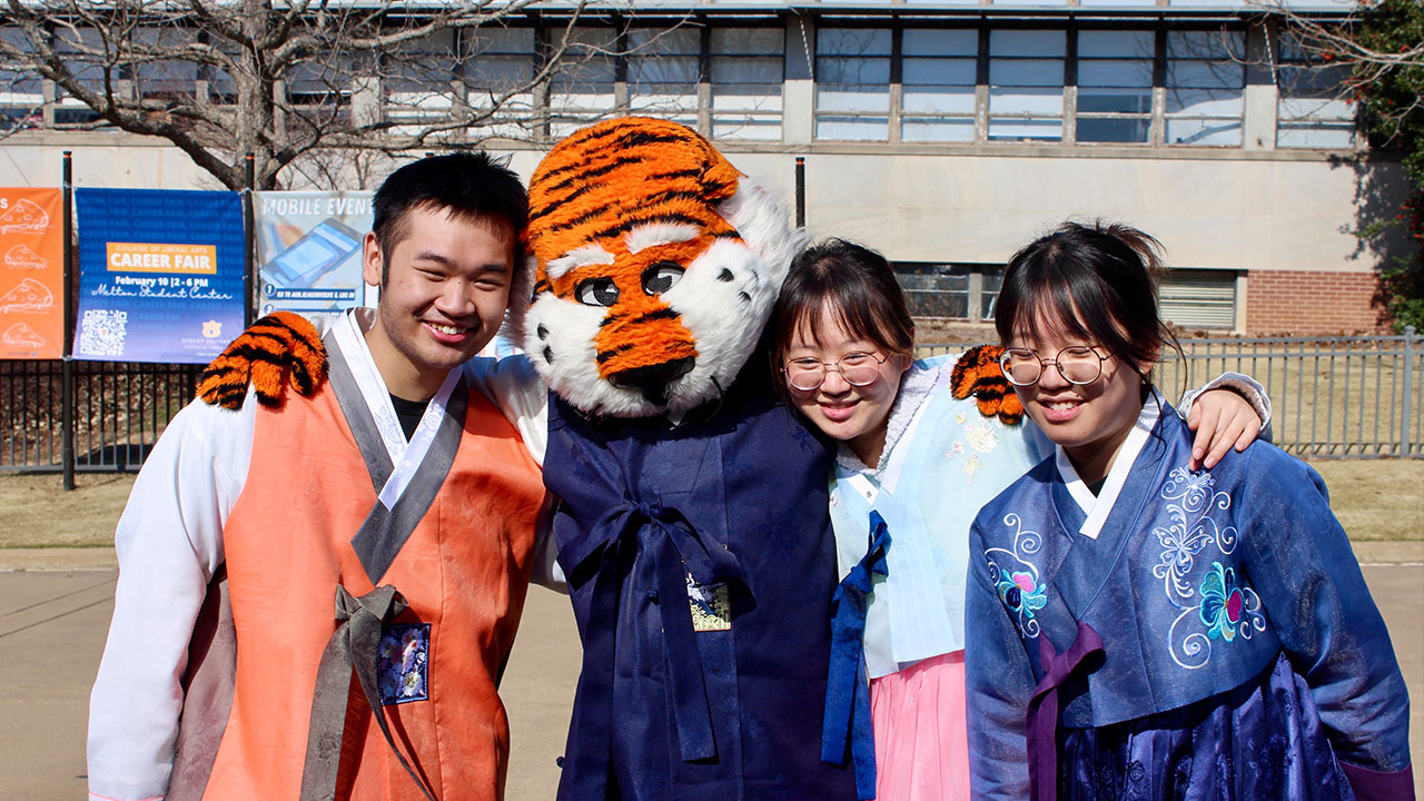 Three students wearing hanboks pose with Aubie
