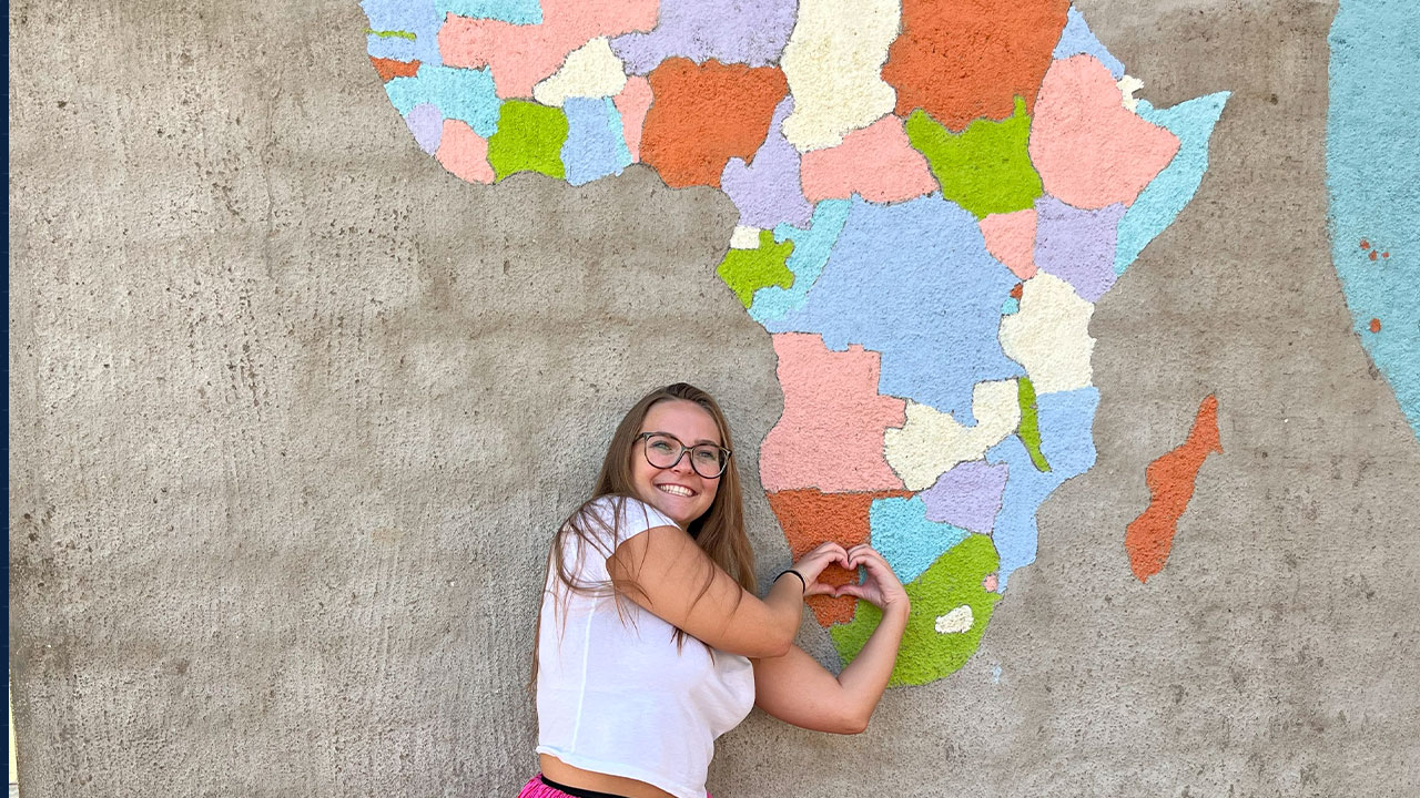 Emma Bradley stands in front of a mural showing the content of Africa