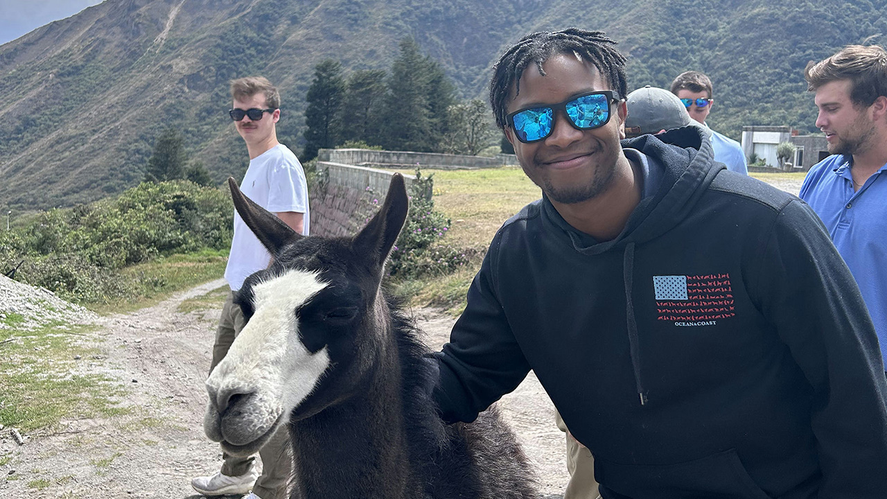A young man poses for a picture with an alpaca as a large mountain looms behind them