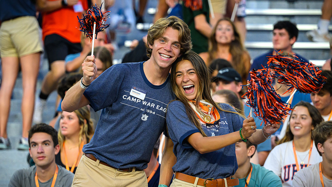 A male and female Camp War Eagle counselor smile and cheer with students behind them.