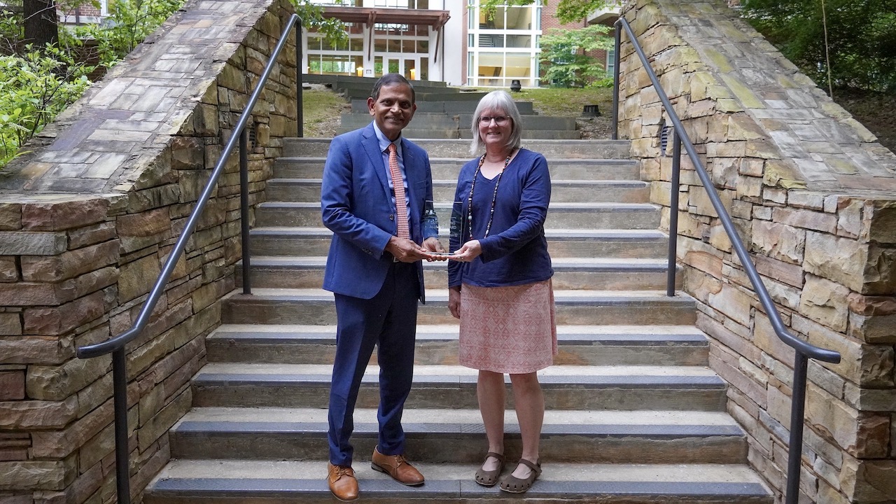 Photo of man and woman holding award on steps outside