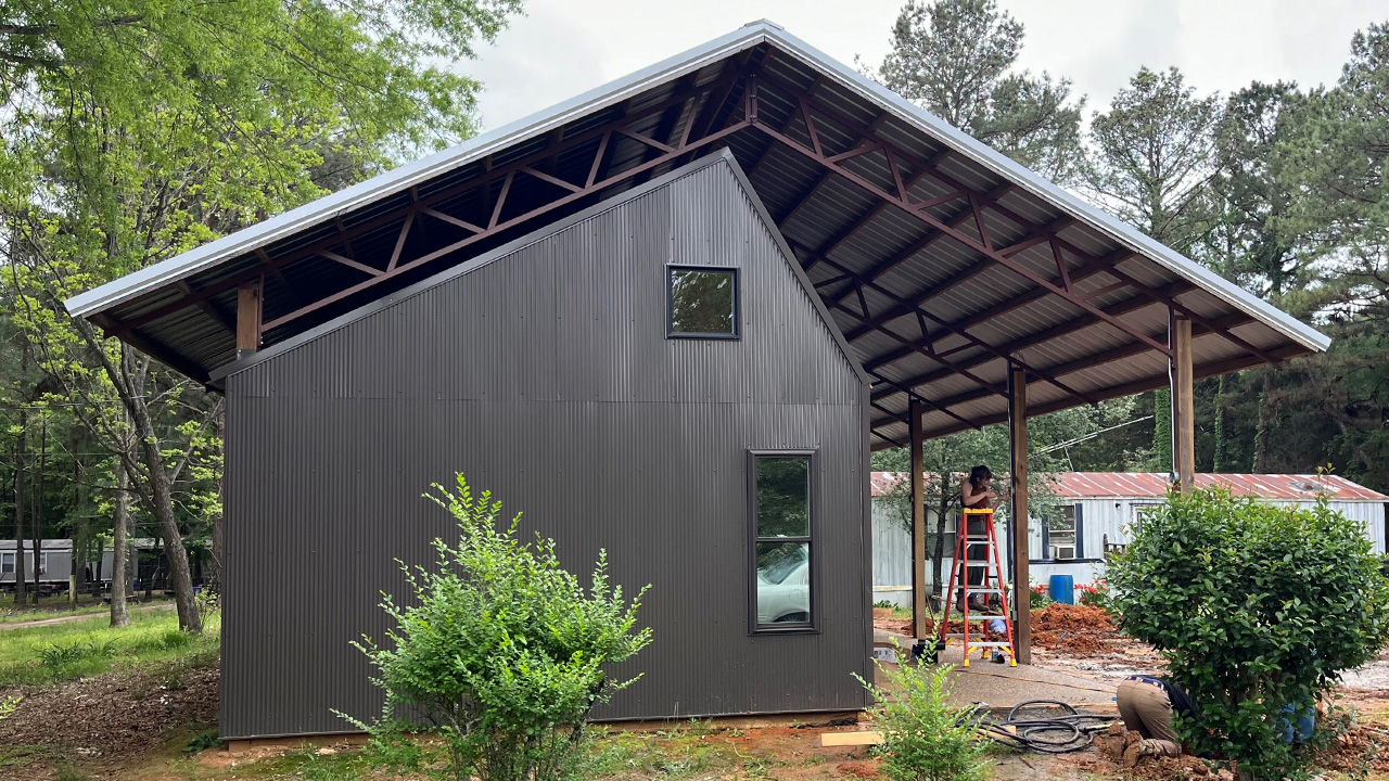 A small house sits underneath a large pole barn
