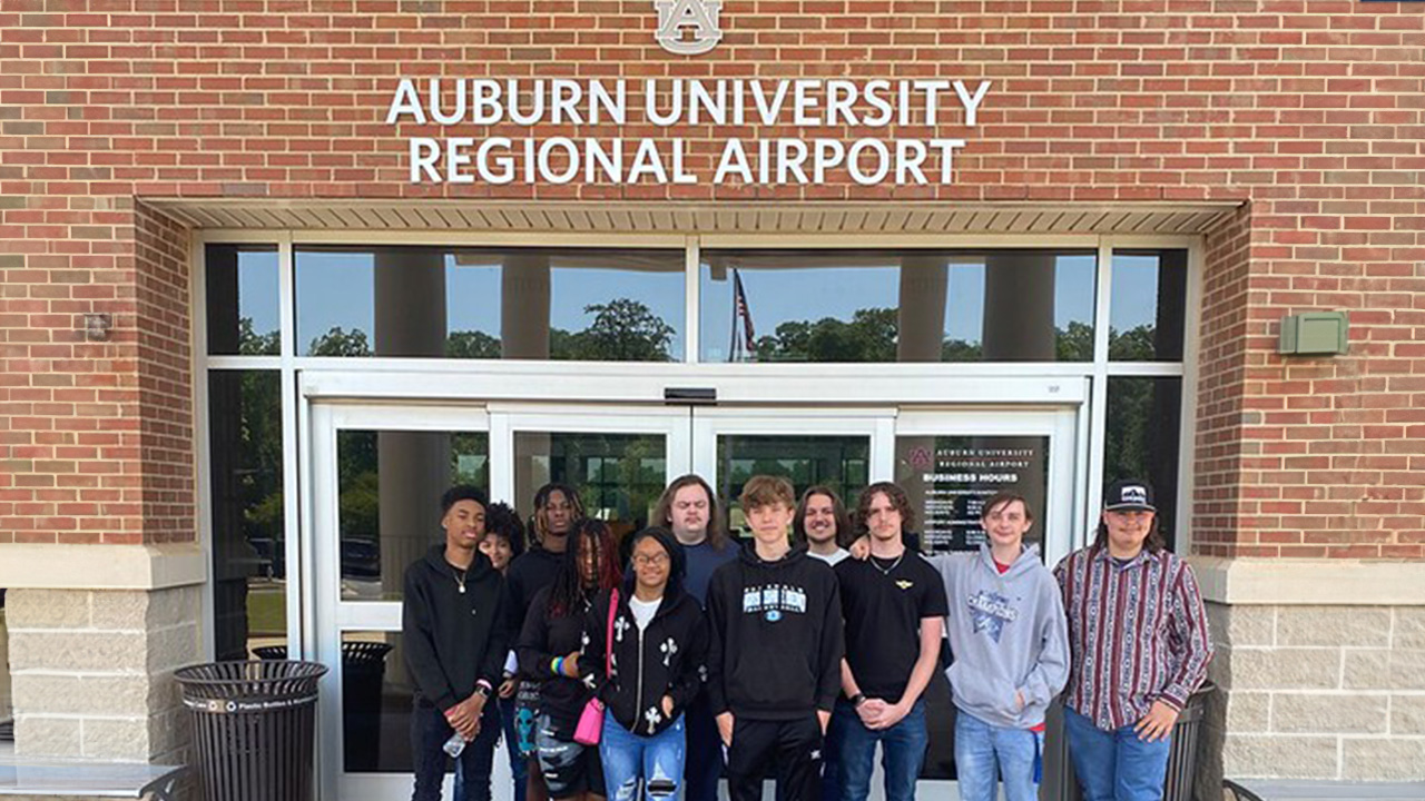 A group of students stand in front of an Auburn University Regional Airport sign