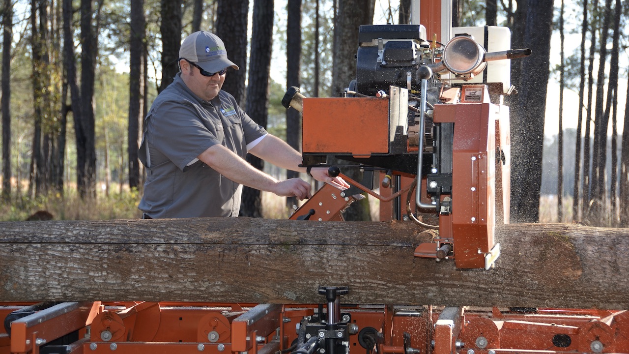 Man saws log outdoors with sawmill
