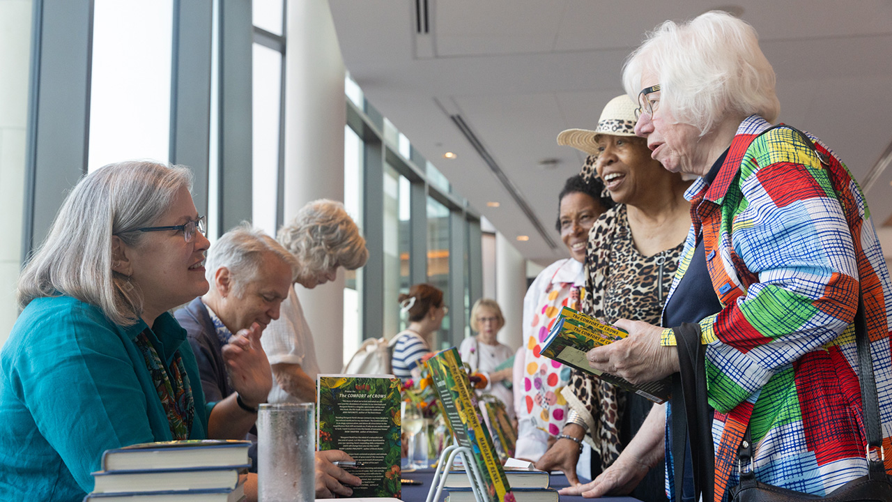 A woman sits at a table and signs books for other women in line