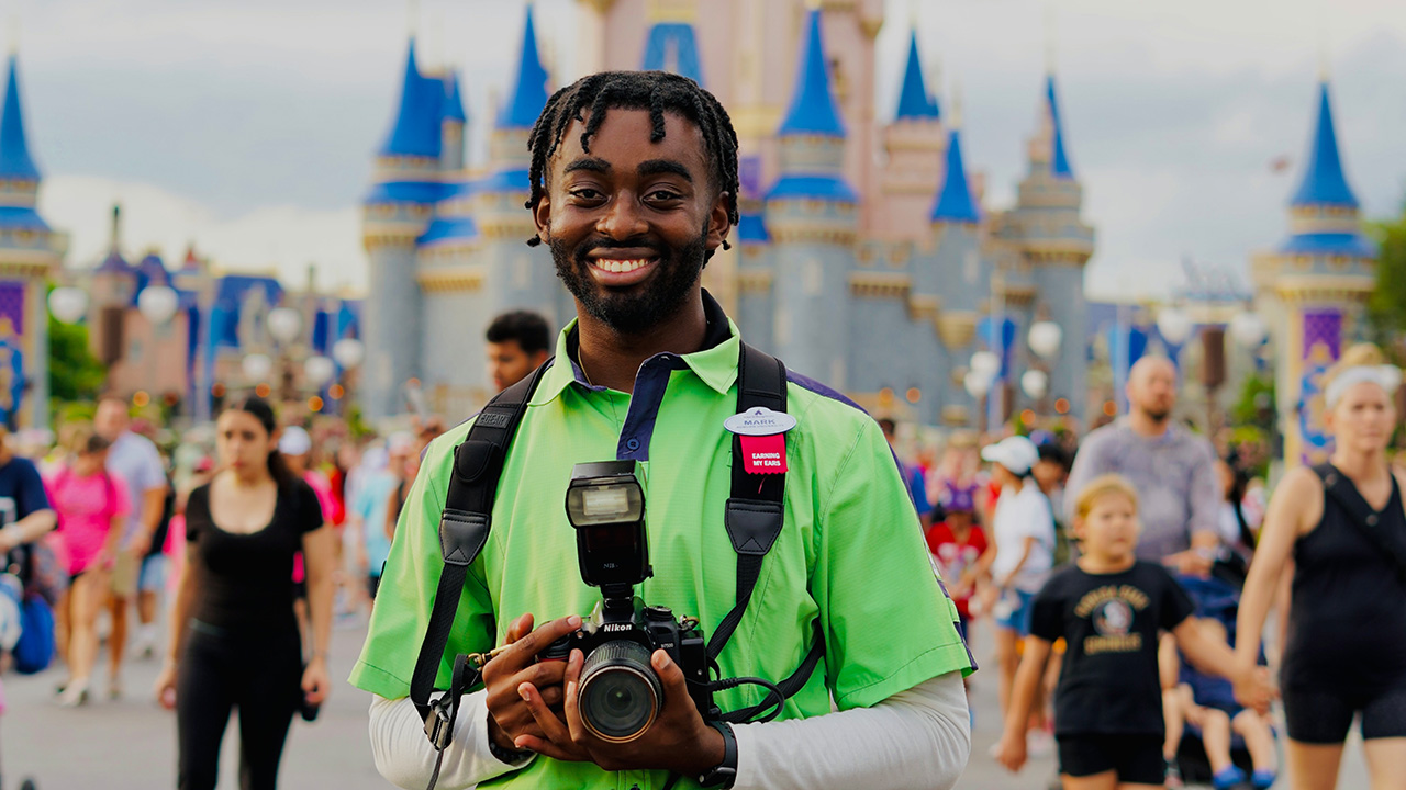 A young man holding a camera stands in front of Cinderella