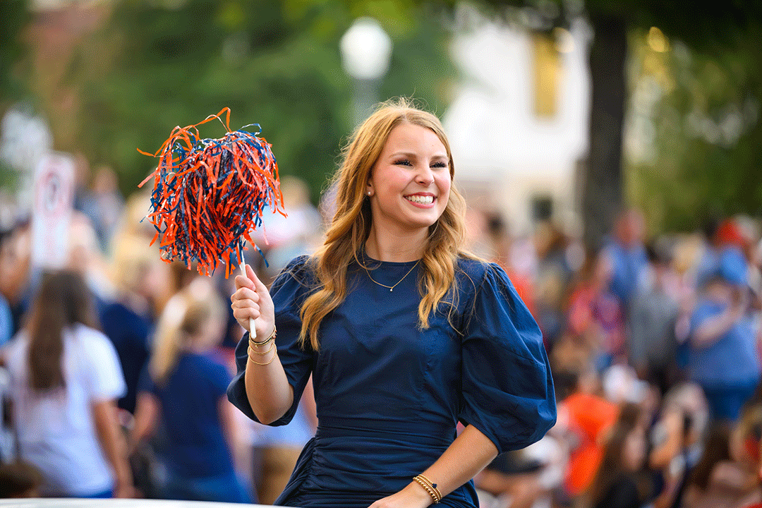A female Auburn student shakes a shaker while sitting in a convertible car.