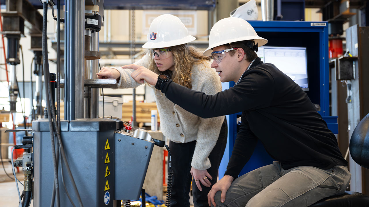 a male and a female student operate a machine in the Advanced Structural Lab