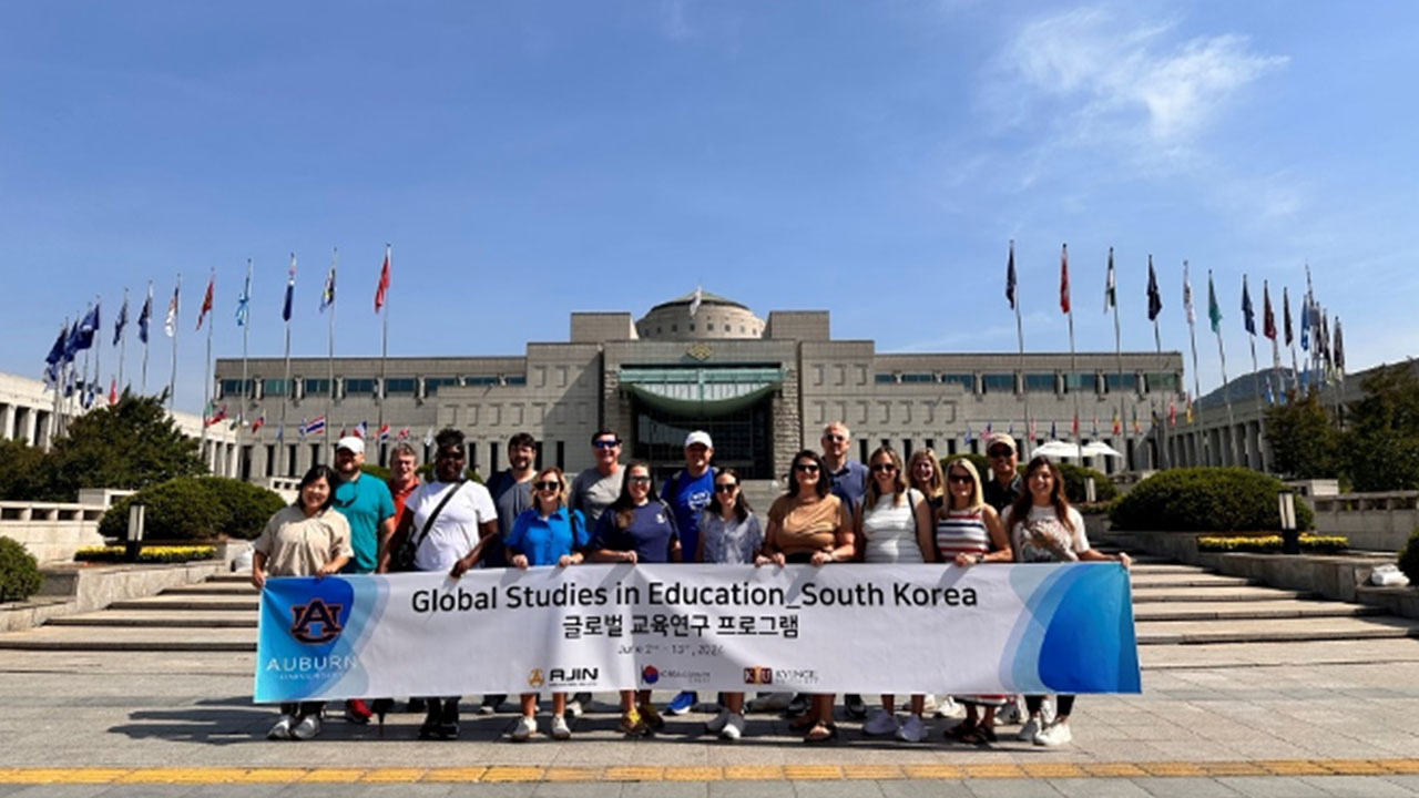 A group of students stand outside a building holding a sign