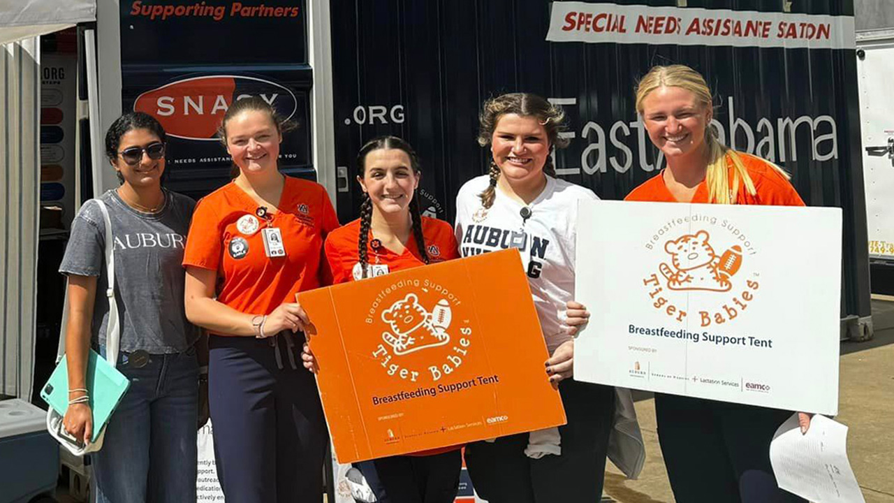 A group of young women hold a sign for the Tiger Babies Breastfeeding Support tent