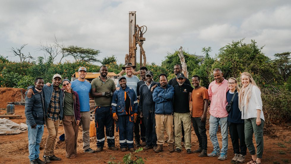 A group of people stands in front of a machine digging a well