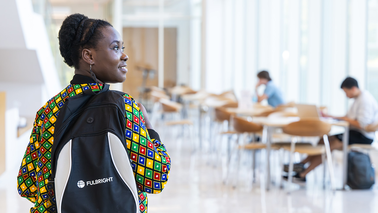 A woman in an African print shirt wears a Fulbright Scholars backpack