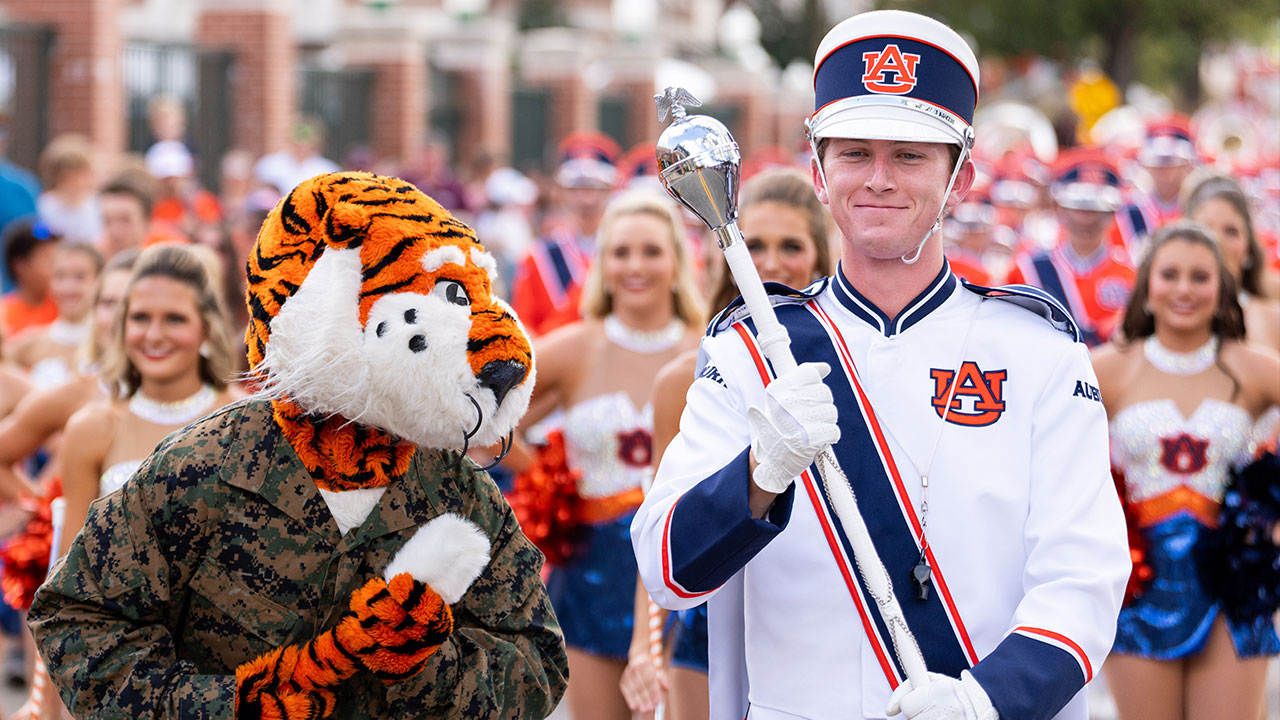 Aubie stands next to Ross Tolbert with the Auburn University Marching Band behind them both.