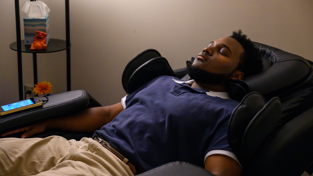 A young man sits in a massage chair with his eyes closed