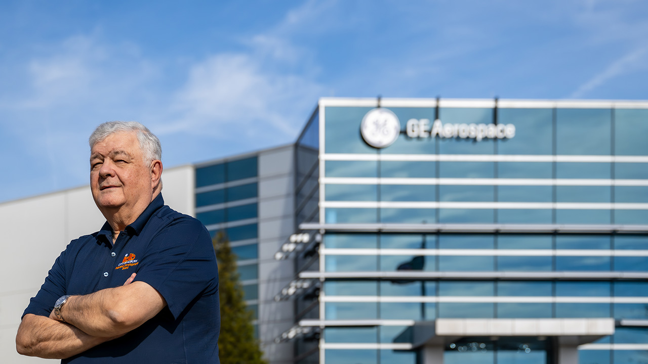 Philip stands in front of a large glass building with his arms crossed