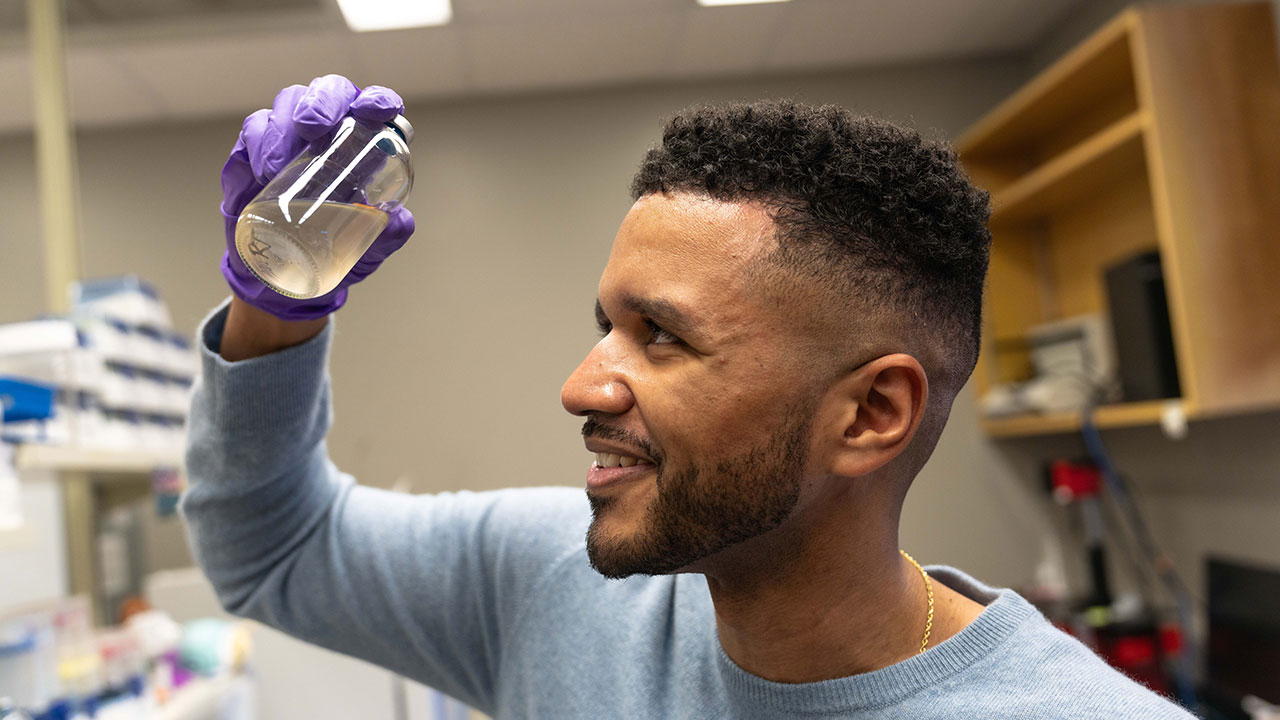 Rodney Tollerson looks at liquid in a glass bottle.