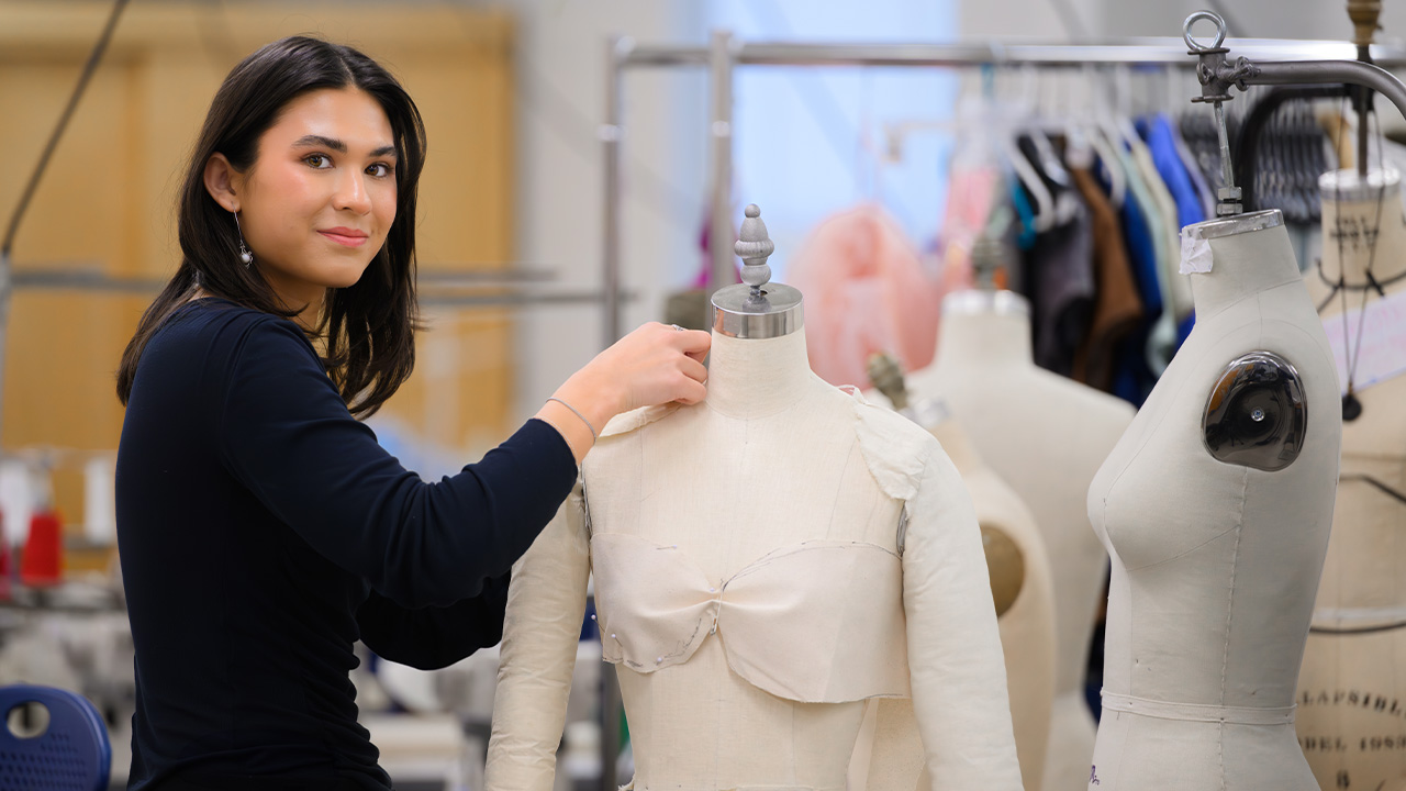 Sydnee smiles as she pins fabric to a form