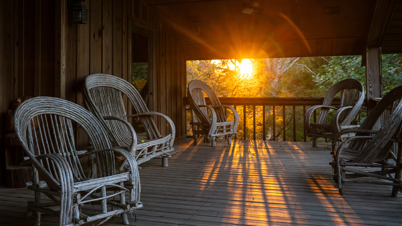 Sunshine shines through the trees on a porch with rustic chairs