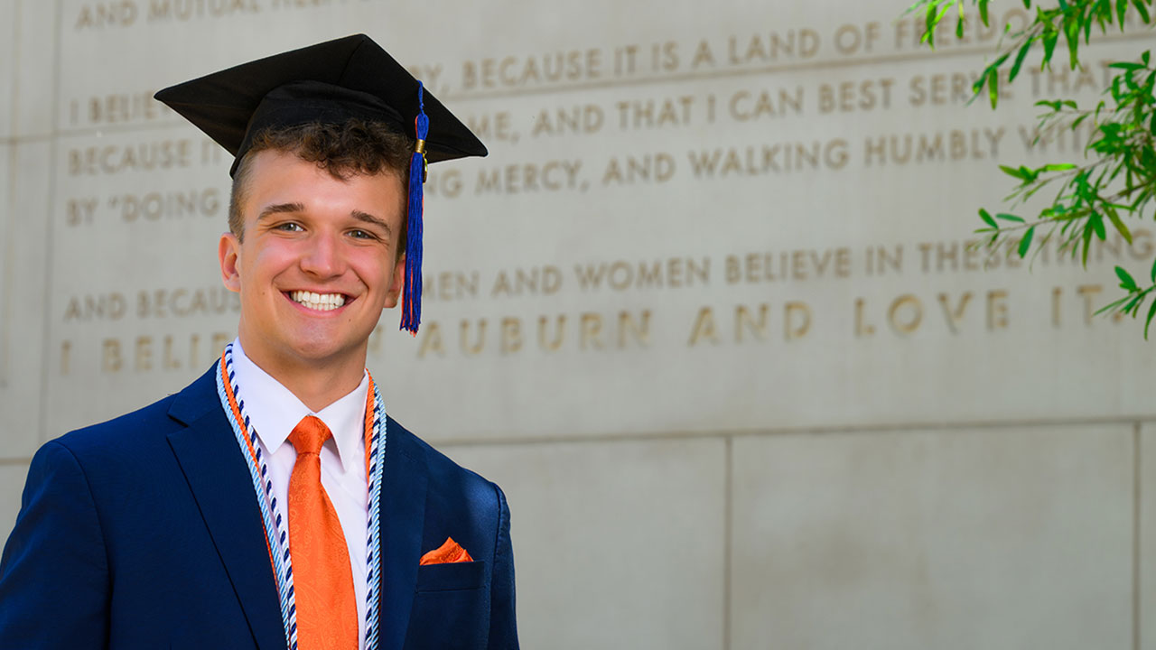 Vince Wolfram in cap and gown in front of the Auburn Creed steps.
