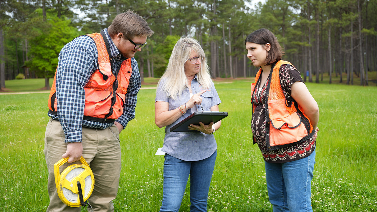 Three people look at a notebook in the woods