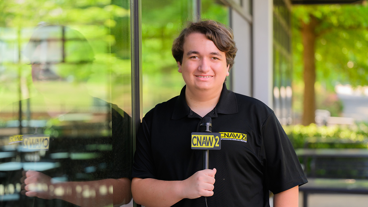 Colin holds a microphone and smiles for the camera