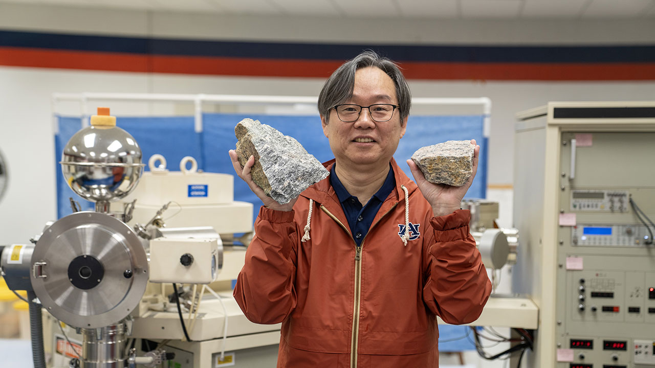 Haibo Zou holding up two rocks in his geology lab.