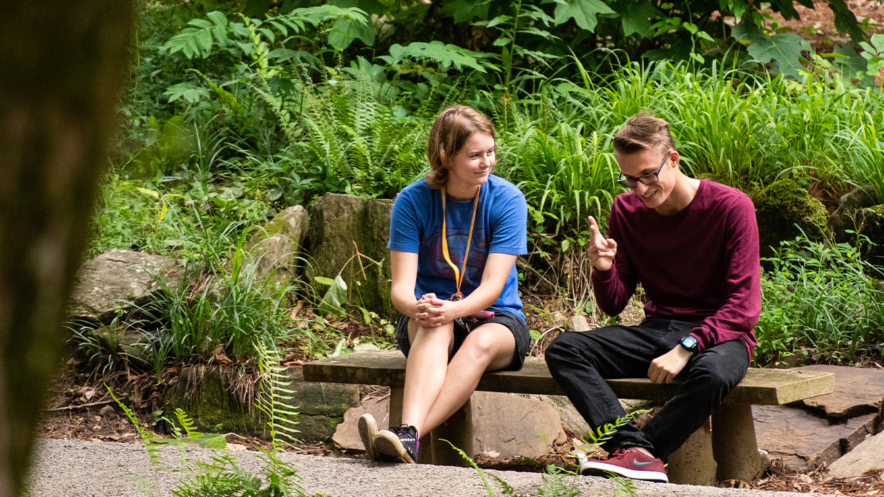Two people sit on a bench in the woods