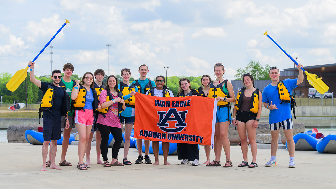 students pose with an Auburn flag after whitewater rafting together