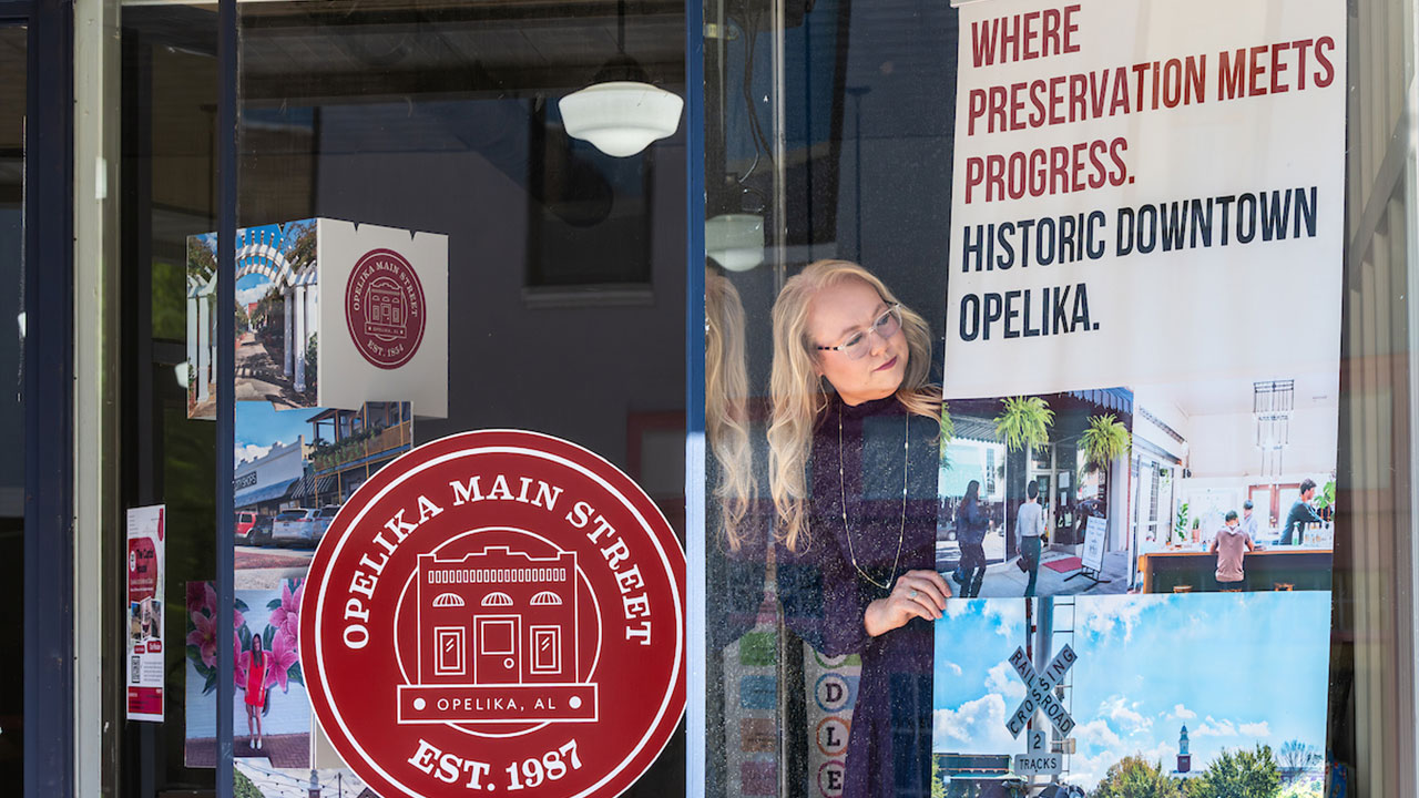 Kelsey Sullivan peers around a banner in the window of the Opelika Main Street office.