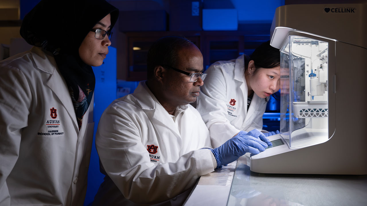 Jay Ramapuram works at a piece of equipment in his lab with two students flanking him.