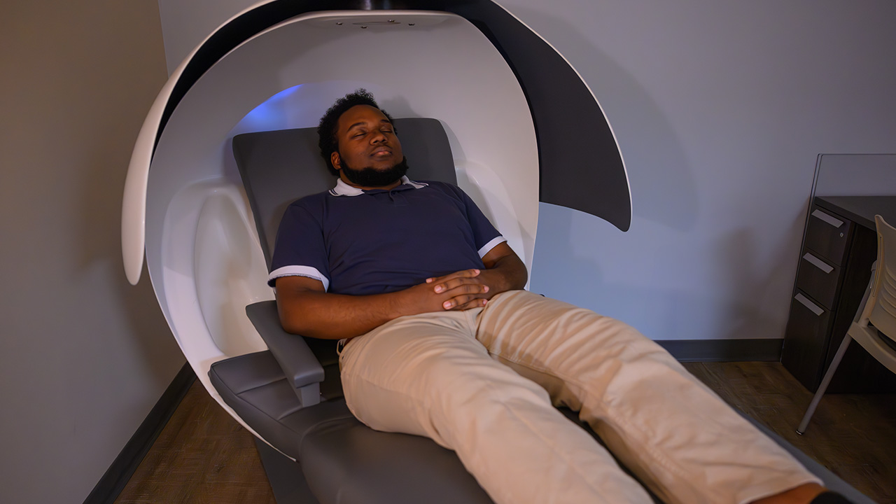 A young man closes his eyes while laying in pod-shaped chair