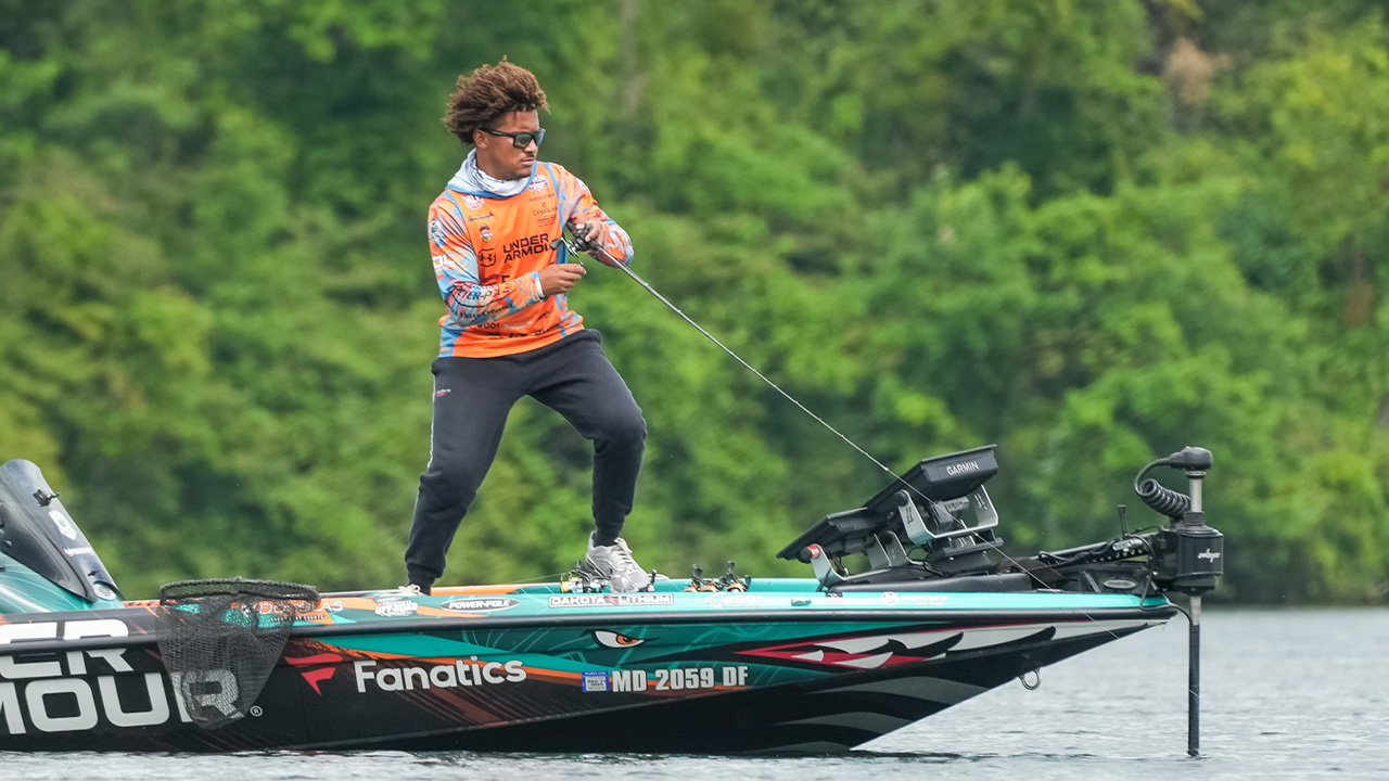 Reece stands on a boat and reels in a fish with a fishing rod