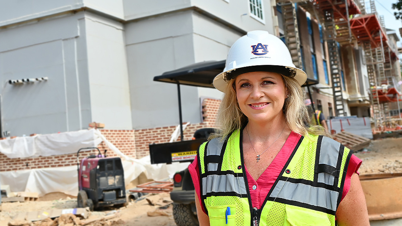 Kelly wears a hard hat and yellow vest on a construction site.